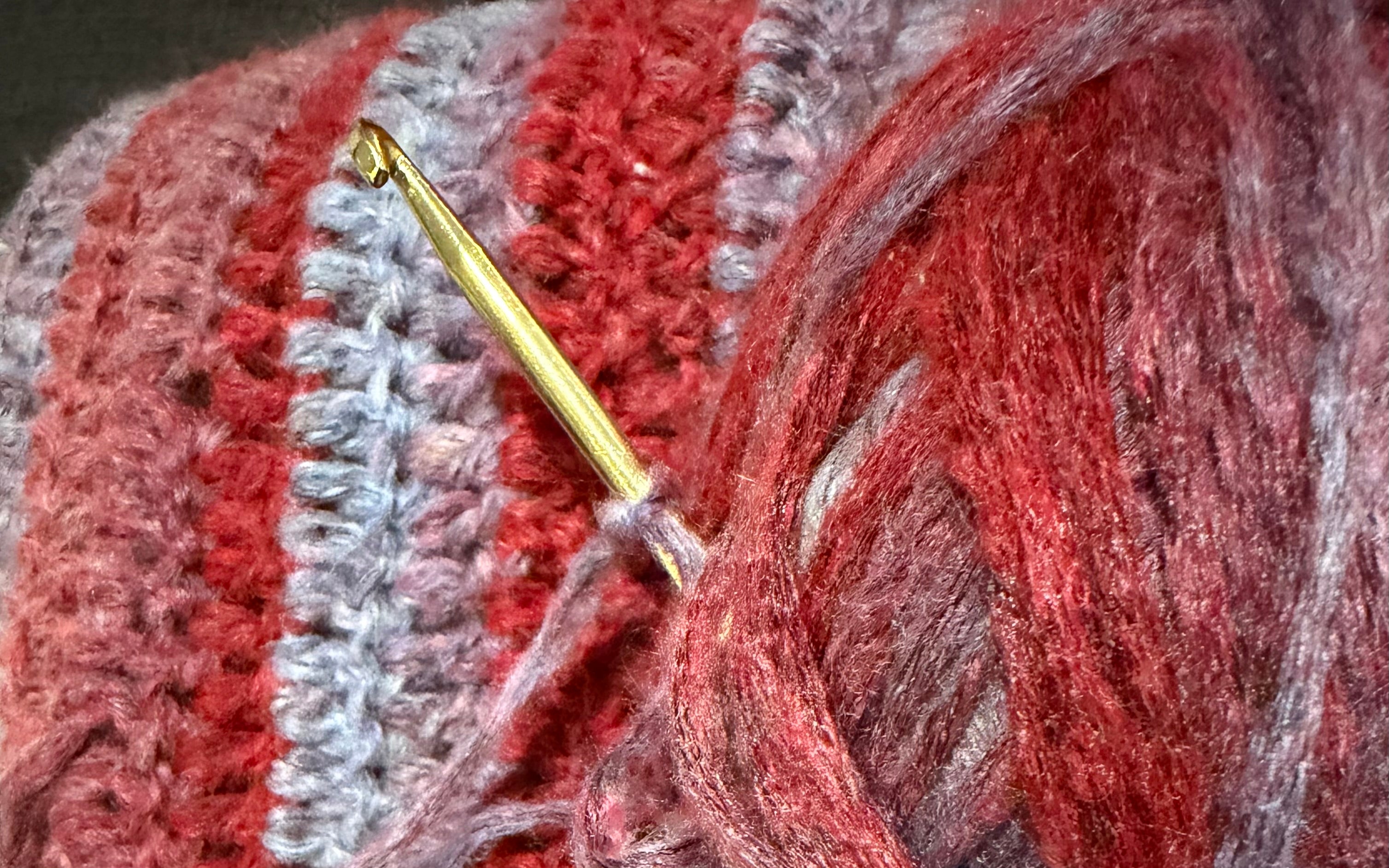 Close-up of a crochet hook inserted into red yarn with a textured fabric background.
